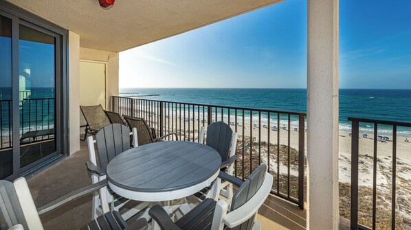 Un balcon avec une table et des chaises, donnant sur une plage, l’océan et une jetée.