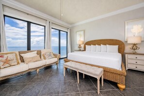 A bedroom with a large bed, a sofa, a bench, and a view of the ocean.