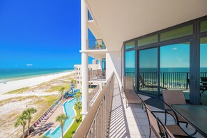 Un balcon avec vue sur la plage et l’océan, une piscine avec des toboggans et un espace extérieur aménagé pour s’asseoir.