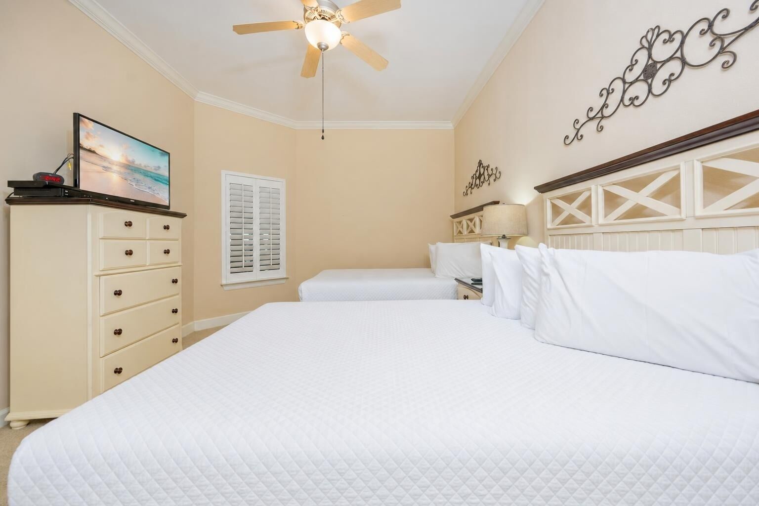 A hotel room with a large bed, a ceiling fan, a dresser, and a wall-mounted TV.