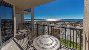 A balcony with a table and chairs, overlooking a beach with a clear sky.