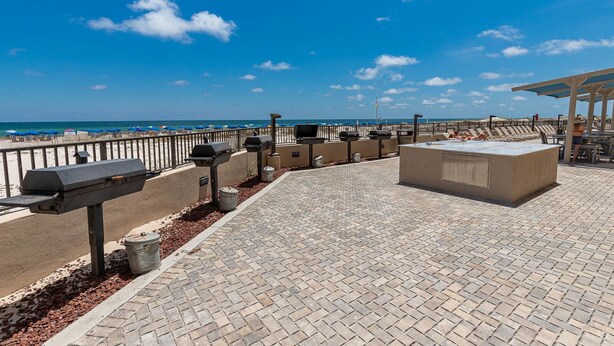 Eine Terrasse im Freien mit Blick auf den Strand, ausgestattet mit Grillanlagen und einer Sitzgruppe.