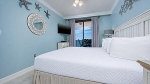 A bedroom with a large bed, a television, a mirror, and a view of the sky through a window.