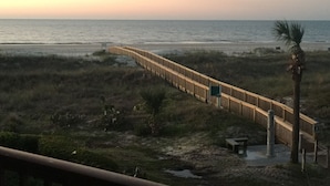 Un muelle de madera que conduce a la playa, rodeado de dunas y vegetación escasa.