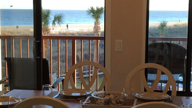 Una mesa de comedor con sillas y vistas a la playa y al océano a través de amplios ventanales.