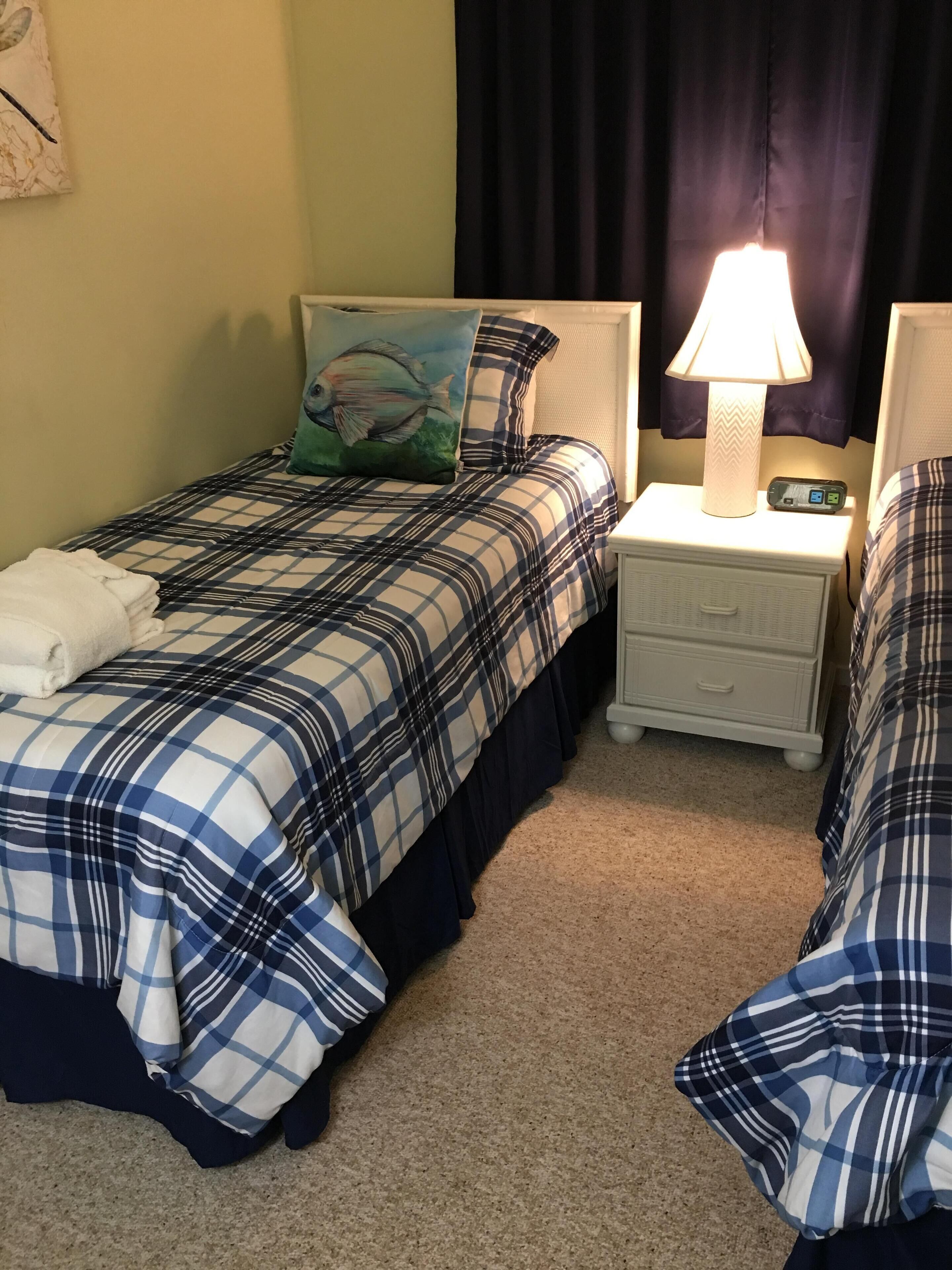 Quarto duplo com cama, mesa de cabeceira, abajur e uma parede com um quadro.