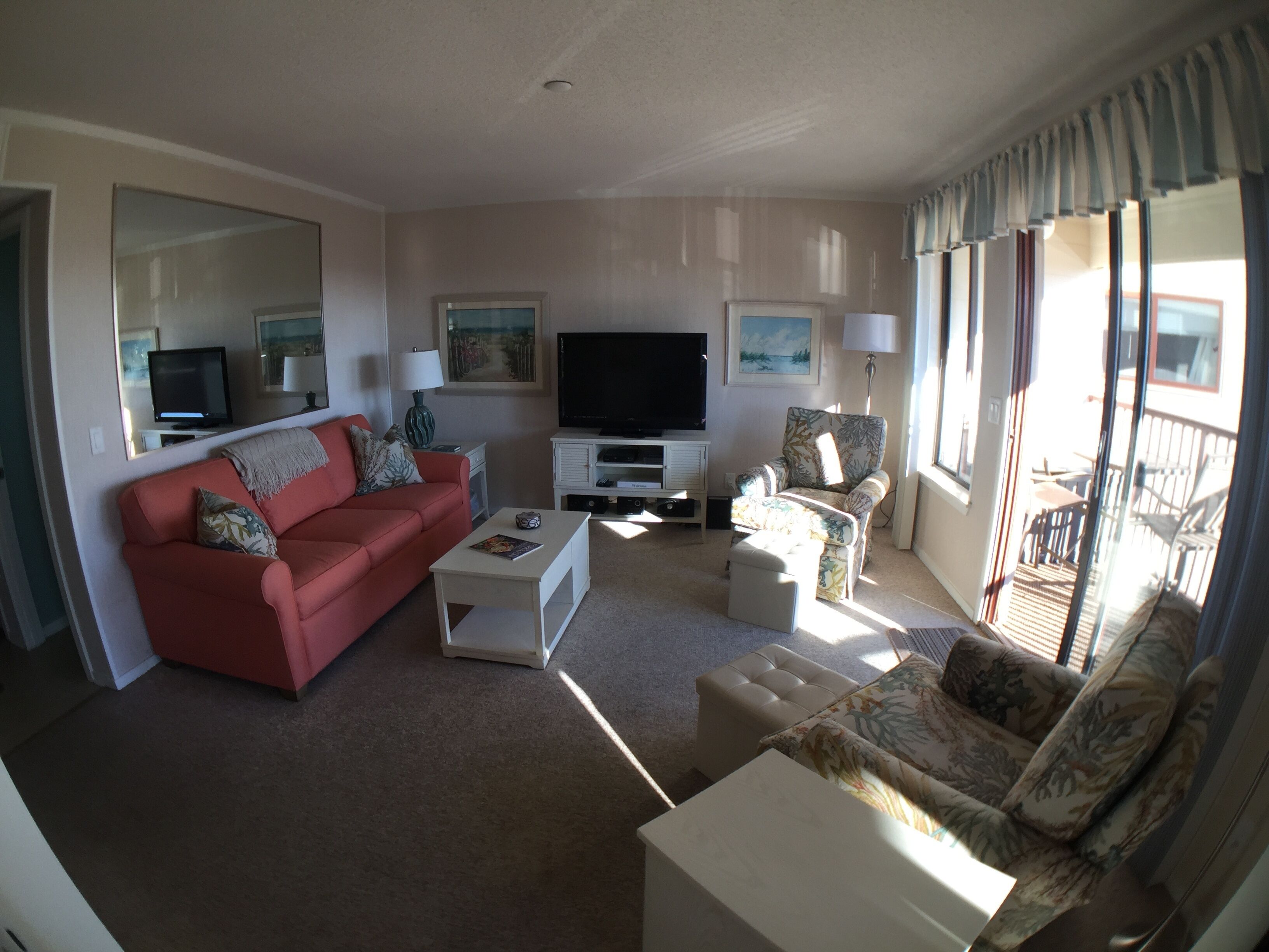 A living room with a red sofa, a white coffee table, a television, and a patterned armchair.