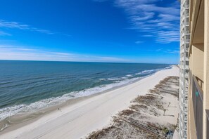 Blick auf einen Strand vom Balkon mit blauem Himmel, Sand und Meer.