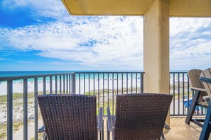 Un balcon avec des fauteuils en osier donnant sur une plage, sous un ciel dégagé.