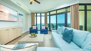 Amplia sala de estar con un ventanal grande con vista al mar, un sofá, dos sillones, una mesa de centro con adornos y un mueble de madera.