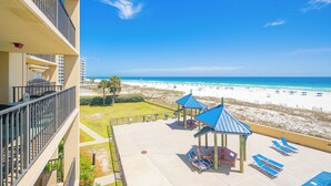 A balcony with a view of a beach, lounge chairs, and a gazebo.