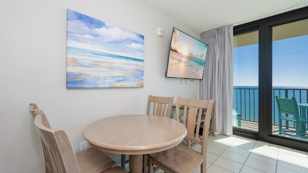 A round wooden table with four chairs, two paintings on the wall, and a balcony with a view of the sea. - SUNSET VIEW ~ Balcony on the BEACH! ~ Phoenix Hotels (Gulf Shores)
