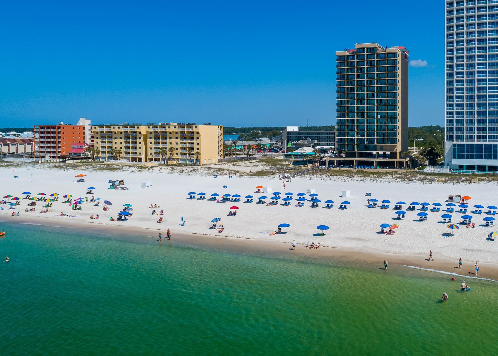 Una playa con numerosas sombrillas y un complejo hotelero al fondo.