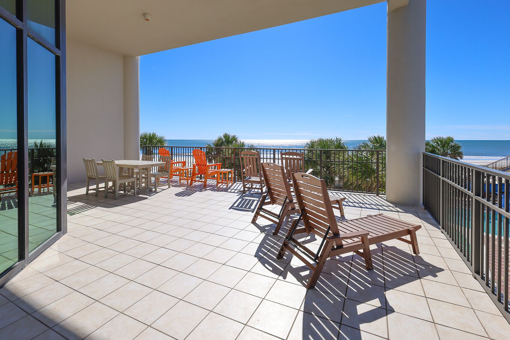Un balcon avec vue sur l’océan, agrémenté de chaises et d’une table en bois.