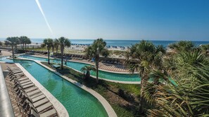 Ein Poolbereich eines Resorts mit mehreren Bahnen, Palmen und einem Strand im Hintergrund.