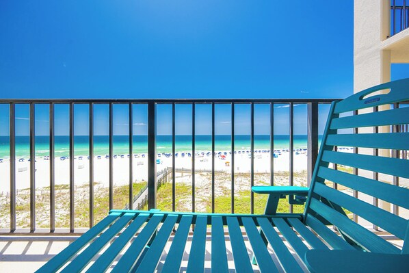 Ein Balkon mit Blick auf einen Strand, ein blauer Stuhl und eine Geländer.