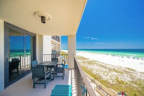 Ein Balkon mit Tisch und Stühlen, eine Glastür mit Blick auf den Strand und einem strahlend blauen Himmel.