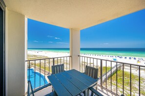 Ein Balkon mit Blick auf Strand und Meer, ein Pool und ein Tisch mit Stühlen.