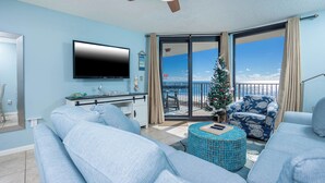 Ein Wohnzimmer mit großem Fernseher, einem Weihnachtsbaum und einem Balkon mit Meerblick.
