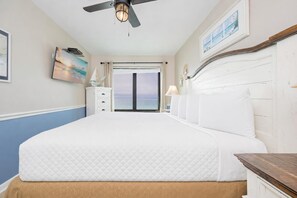Une chambre avec un grand lit, un ventilateur de plafond, une vue sur l’océan et une commode blanche.