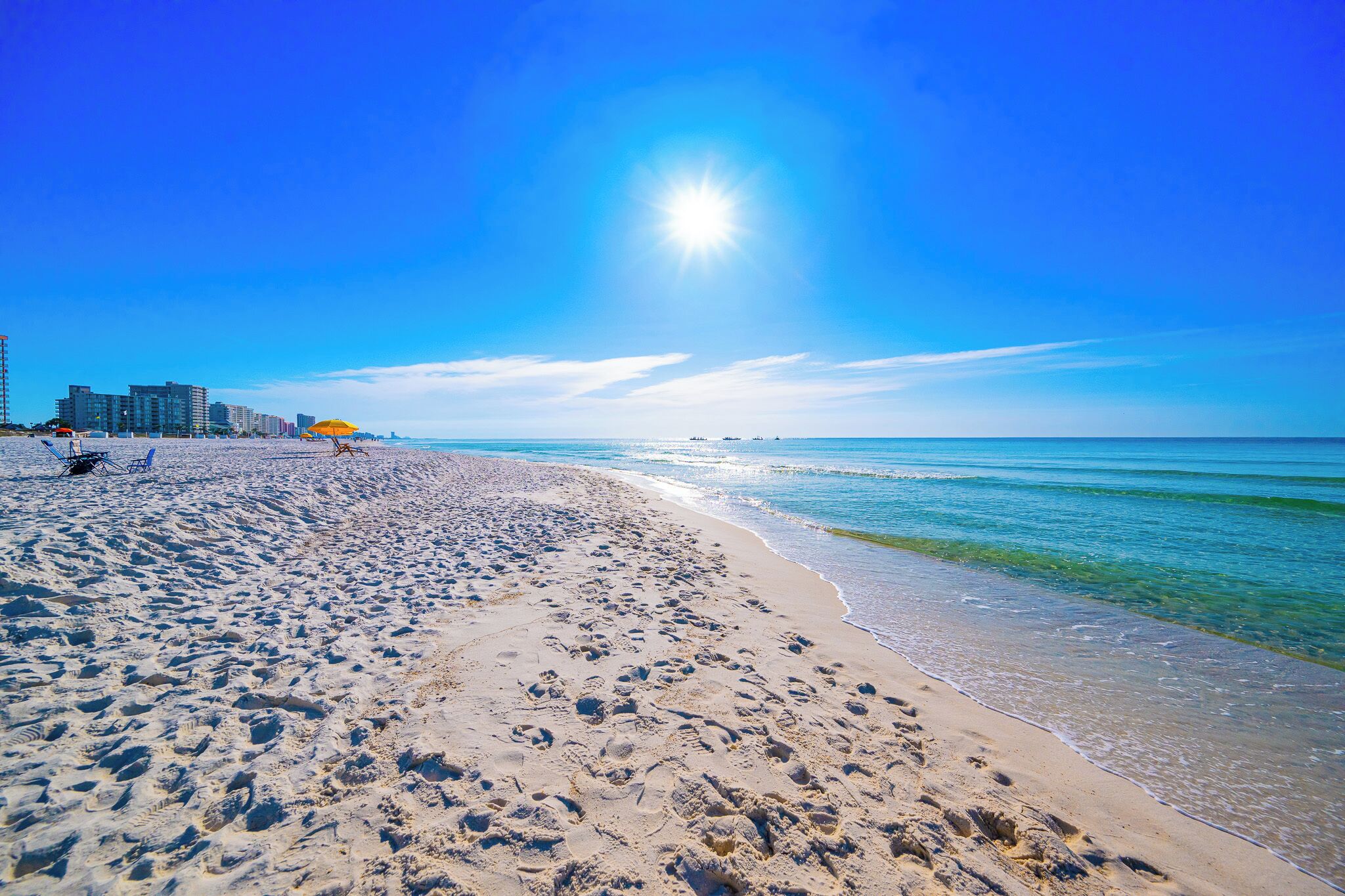 A beach with footprints, a clear sky, and buildings in the background.