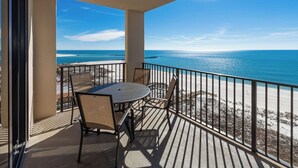 A balcony with a table and chairs overlooking a beach. - ~ 2BR @ Phoenix East (Orange Beach)