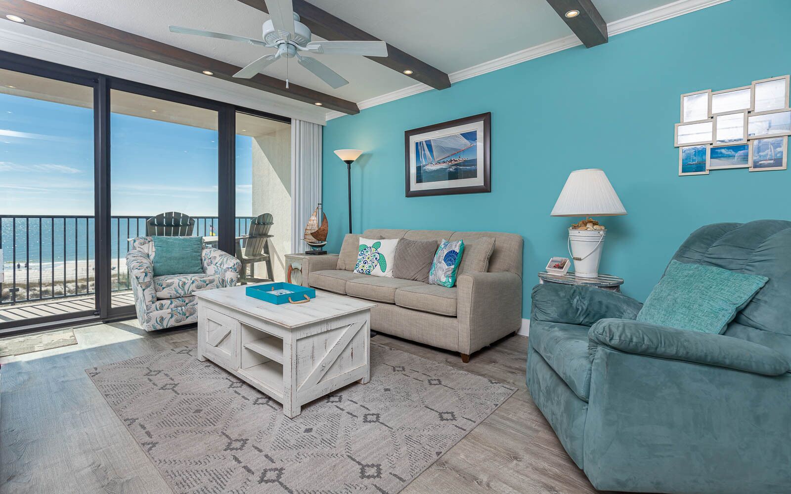A living room with a view of the beach, a ceiling fan, a sofa, a chair, and a coffee table.