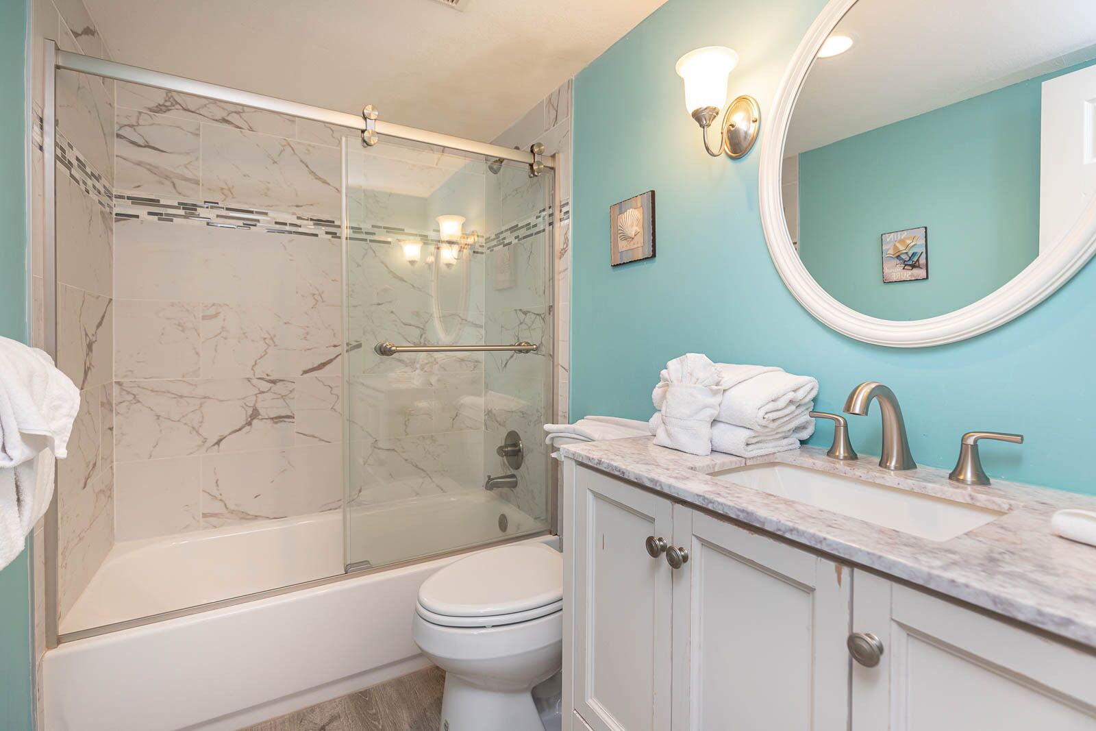 A bathroom with a glass-enclosed shower, a white toilet, a marble-topped sink, and a teal wall.