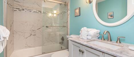 A bathroom with a glass-enclosed shower, a white toilet, a marble-topped sink, and a teal wall.
