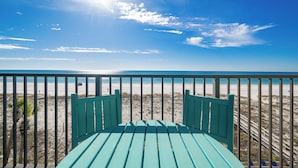 A beach view from a balcony with a green chair and a railing.