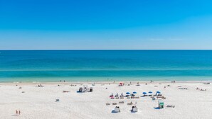 Une vaste plage avec une eau d’un bleu limpide, de nombreux parasols et des gens qui se détendent.
