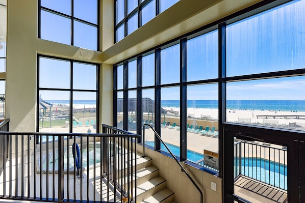 Enjoy expansive ocean views from the large windows in this spacious room, featuring a curved staircase leading to a pool area.