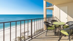Un balcon avec vue sur une plage et l’océan. On y trouve des chaises en osier et une petite table ronde.