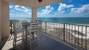 A balcony with a table and chairs overlooking a beach with a clear sky. - Two Bedroom Condo in HIGH DEMAND! Phoenix East! (Orange Beach)