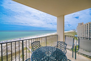 A balcony with a view of the beach and ocean, a round table, and two chairs.