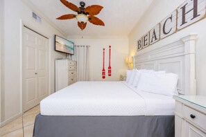 A hotel room with a bed, a wardrobe, a ceiling fan, a painting, and a sign with the word 'BEACH'.