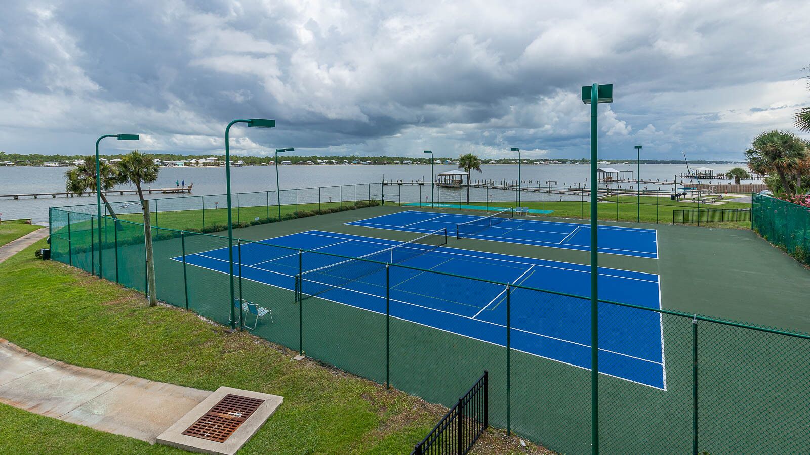 A tennis court with a surrounding fence, a grassy area, and a view of a body of water.