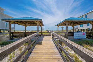 Ein hölzerner Steg führt zu Strandhütten, mit einem Schild für den Gulf Shores Surf & Racquet Club.