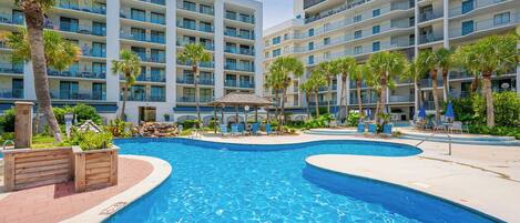 A hotel with multiple balconies, a swimming pool, and palm trees.