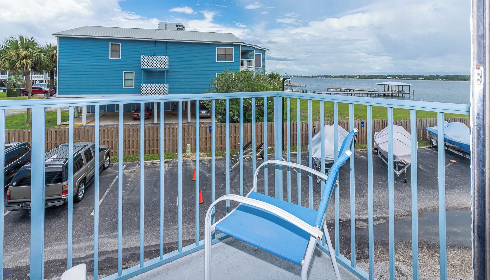 A blue building with a fenced parking area, a covered boat dock, and a view of the water.
