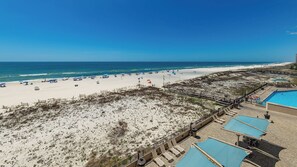 A beach view with a pool area, lounge chairs, and umbrellas. - 4th Floor Two Bedroom Condo 415 at Phoenix 10 (Orange Beach)