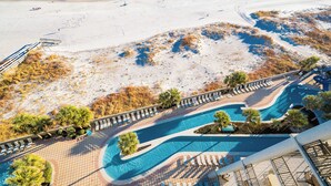 Vue aérienne d’un complexe hôtelier de bord de mer, avec une piscine, des transats et une zone de plage.