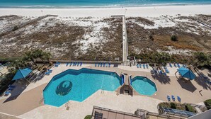 Ein großer, offener Pool mit mehreren Bahnen, umgeben von Liegestühlen und Sonnenschirmen. Im Hintergrund ein Strand und Dünen.