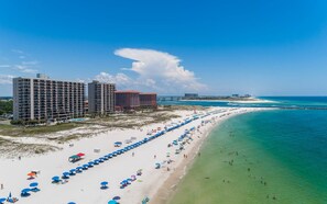 Un complejo turístico en la playa con varios edificios altos, una extensa orilla con sombrillas y aguas turquesas cristalinas.