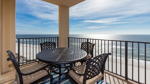 Ein Balkon mit rundem Tisch und vier Stühlen mit Blick auf einen Strand und den Ozean.
