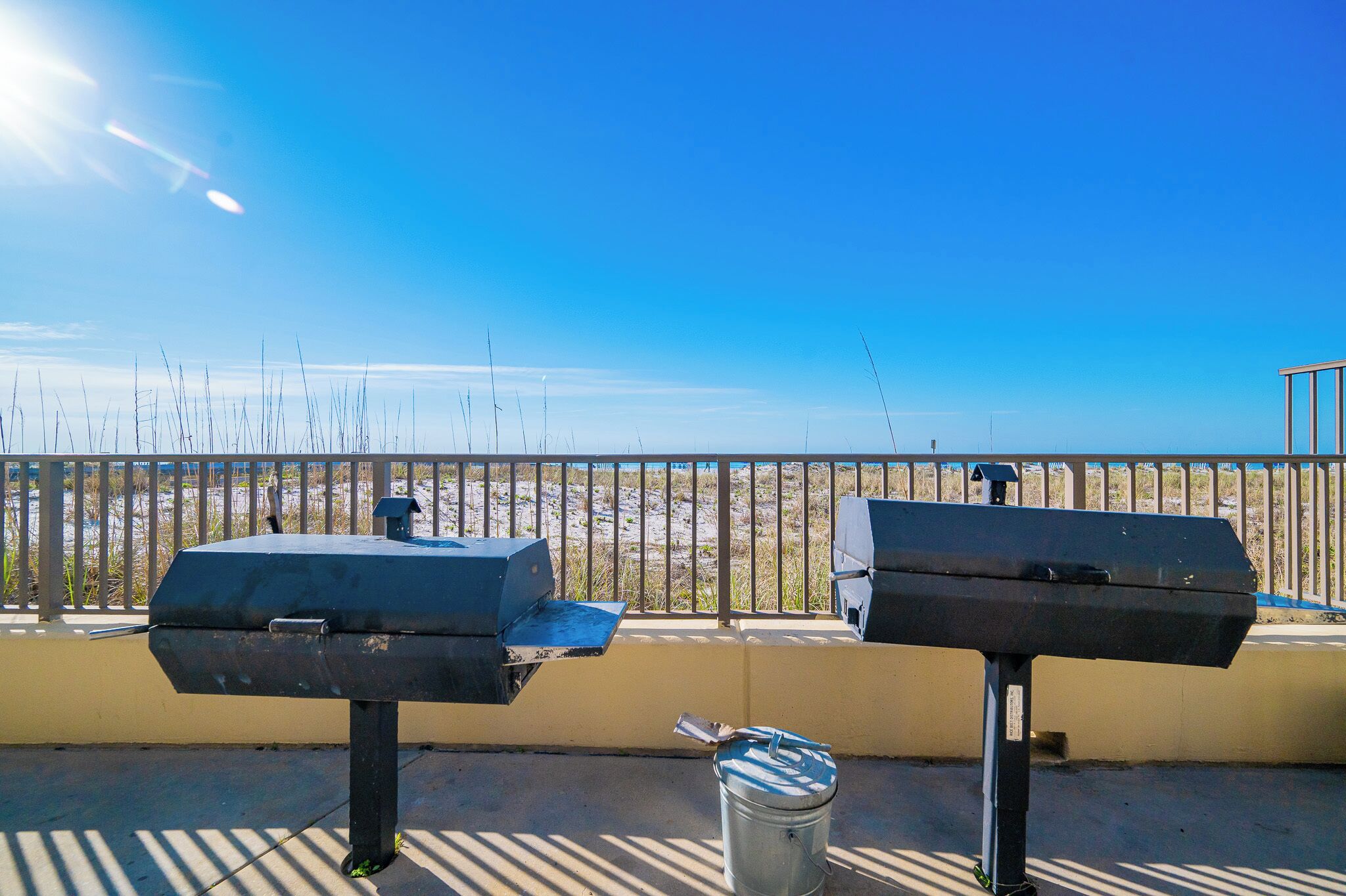 Two barbecue grills on a balcony with a view of the beach.