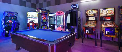A pool table in a room with arcade games and a photo booth.