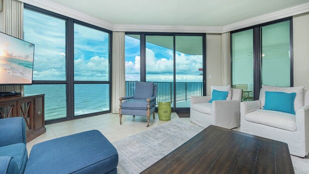 Ein geräumiger Balkon mit Blick aufs Meer, ausgestattet mit einem blauen Sessel, einem weißen Sofa mit blauen Kissen und einem Holztisch.