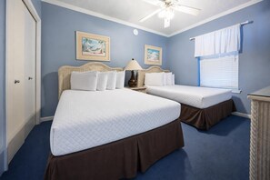 Une chambre avec deux lits, un ventilateur de plafond et deux tableaux encadrés accrochés au mur.