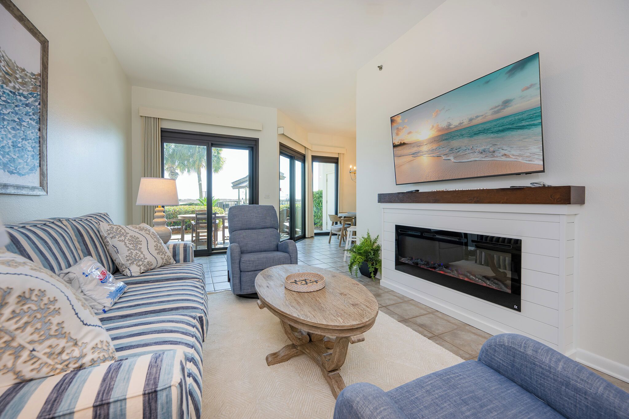 A living room with a sofa, armchair, fireplace, and a large TV on the wall.